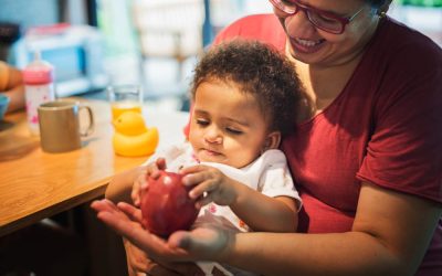 Mère souriante tenant son bébé sur les genoux pendant le repas, illustrant le soutien familial et la pension alimentaire.