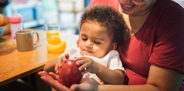 Mère souriante tenant son bébé sur les genoux pendant le repas, illustrant le soutien familial et la pension alimentaire.