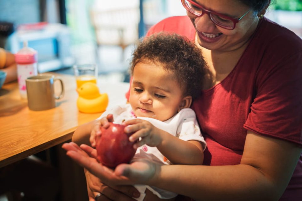 Mère souriante tenant son bébé sur les genoux pendant le repas, illustrant le soutien familial et la pension alimentaire.