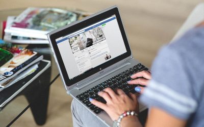 Une personne utilise un ordinateur portable avec une page web visible, des magazines sont empilés à côté