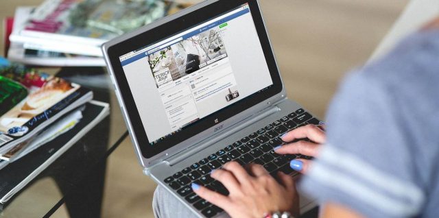 Une personne utilise un ordinateur portable avec une page web visible, des magazines sont empilés à côté