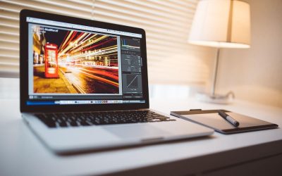 Un ordinateur portable sur un bureau, une lampe allumée, une photo en cours d'édition
