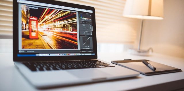 Un ordinateur portable sur un bureau, une lampe allumée, une photo en cours d'édition