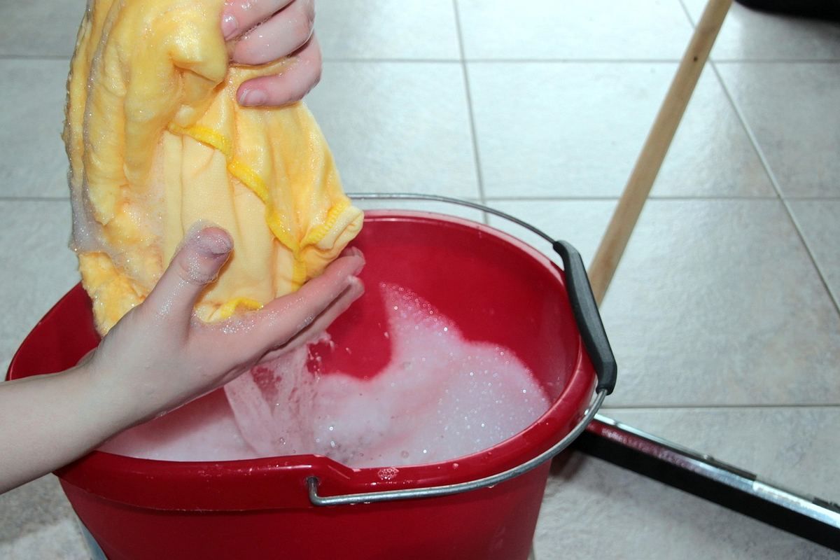 Personne plongeant un linge jaune dans un seau d'eau rouge pour le nettoyer