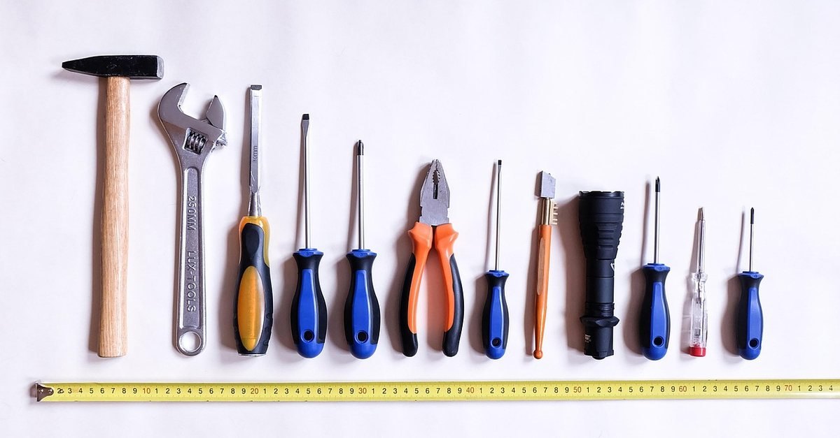 Une rangée d'outils de bricolage posés sur fond blanc, mesurés par une règle