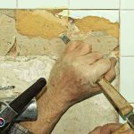Une main utilise un marteau et un burin pour enlever une tuile
