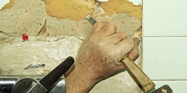 Une main utilise un marteau et un burin pour enlever une tuile