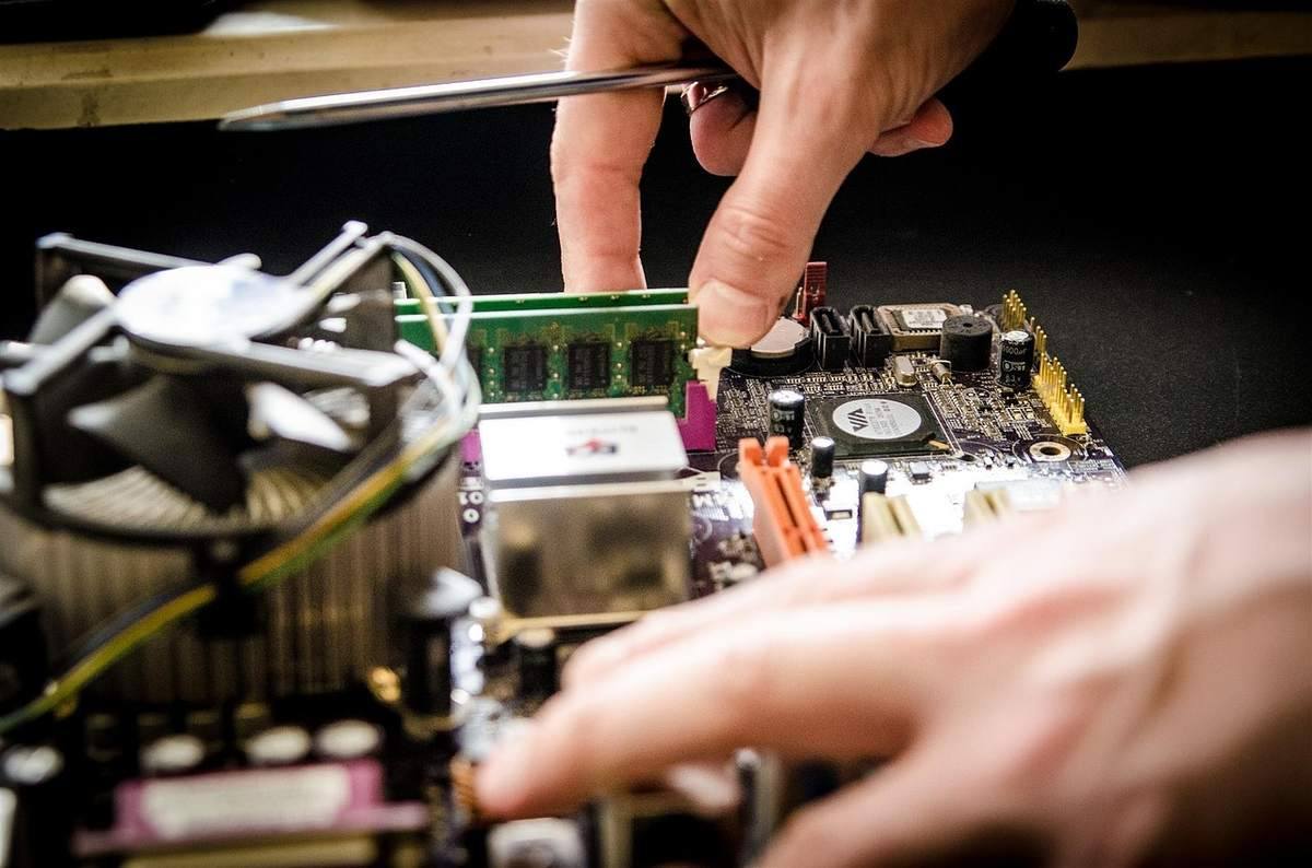 Une main installe une barrette RAM sur une carte mère avec un ventilateur