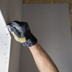 Une main gantée applique de la pâte à joint sur un mur blanc