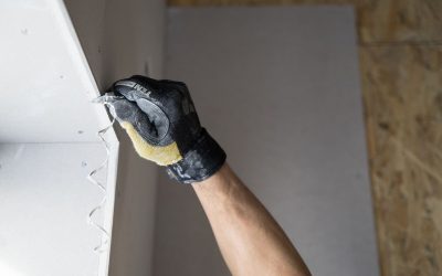 Une main gantée applique de la pâte à joint sur un mur blanc