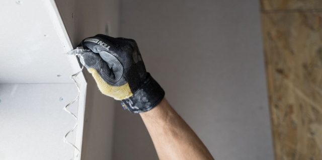 Une main gantée applique de la pâte à joint sur un mur blanc