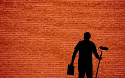 Un homme en noir tient un rouleau et un seau contre un mur rouge