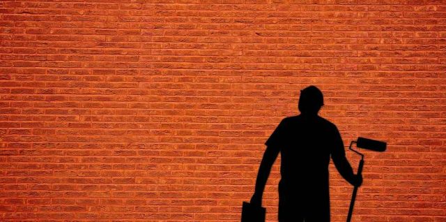 Un homme en noir tient un rouleau et un seau contre un mur rouge